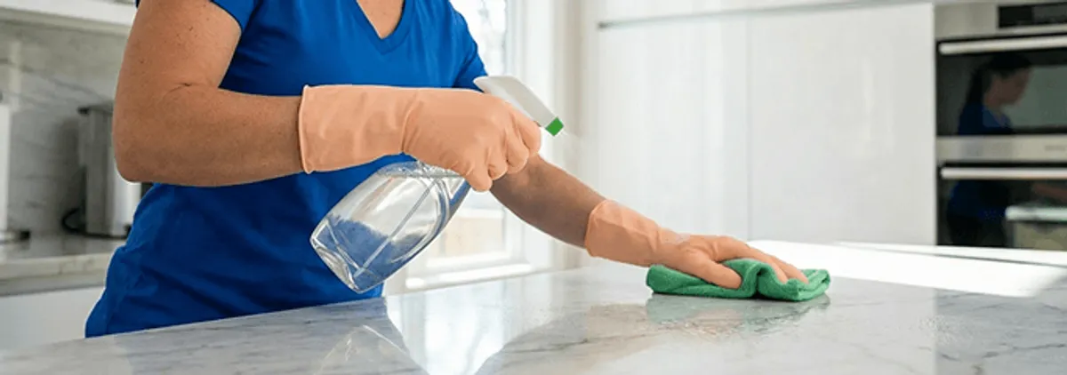 Maid service worker spraying and wiping a kitchen countertop with a microfiber cloth for sanitizing, Springfield, MO.